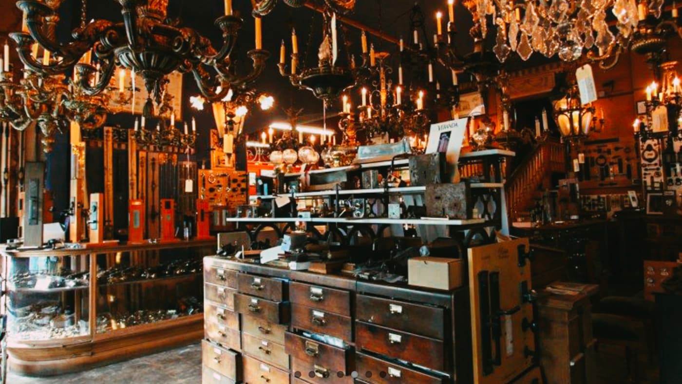 Interior of the Architectural Accents showroom featuring a dense display of antique brass chandeliers, ornate crystal light fixtures, and vintage hardware organized in a series of dark wood apothecary-style drawers.