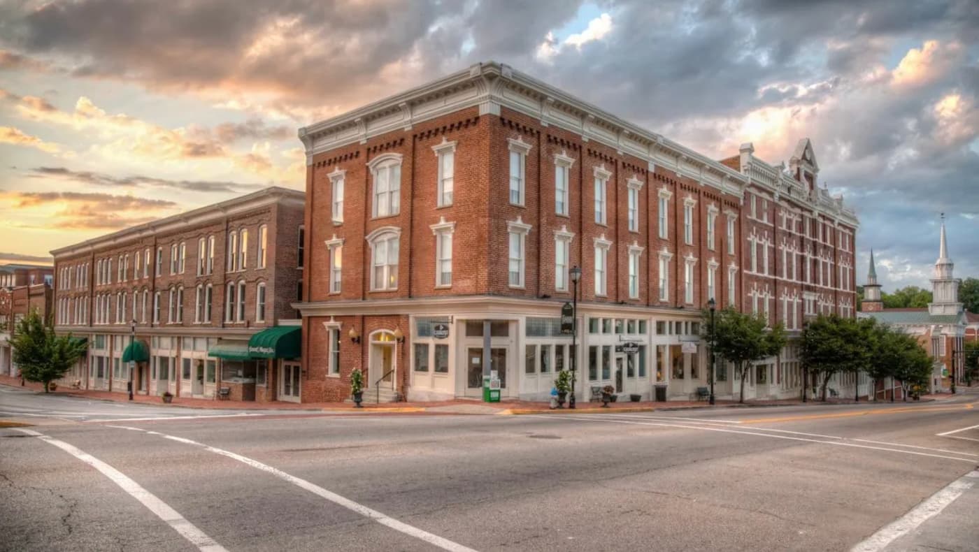 Exterior front view of the General Morgan Inn and Conference Center in historic Greeneville, TN. The grand four-story red brick hotel features a symmetrical facade with a prominent central entrance under a dark green awning.