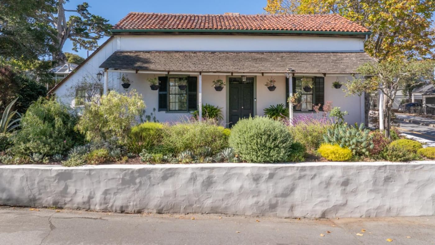 Alt text: Exterior view of Casa de la Torre in Monterey, CA, a 19th-century historic adobe home featuring traditional white-washed walls, a low-slung roof, and a unique large rounded window added in the 1920s.