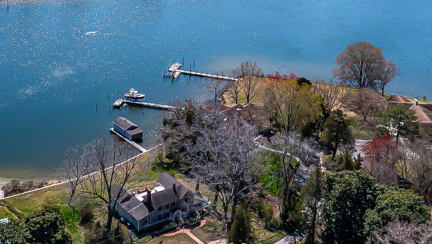 Alt text: A historic steamboat-era white siding home, Captain’s Quarters, situated on a lush one-acre lawn leading to the shores of Carter’s Creek in Irvington, Virginia.
