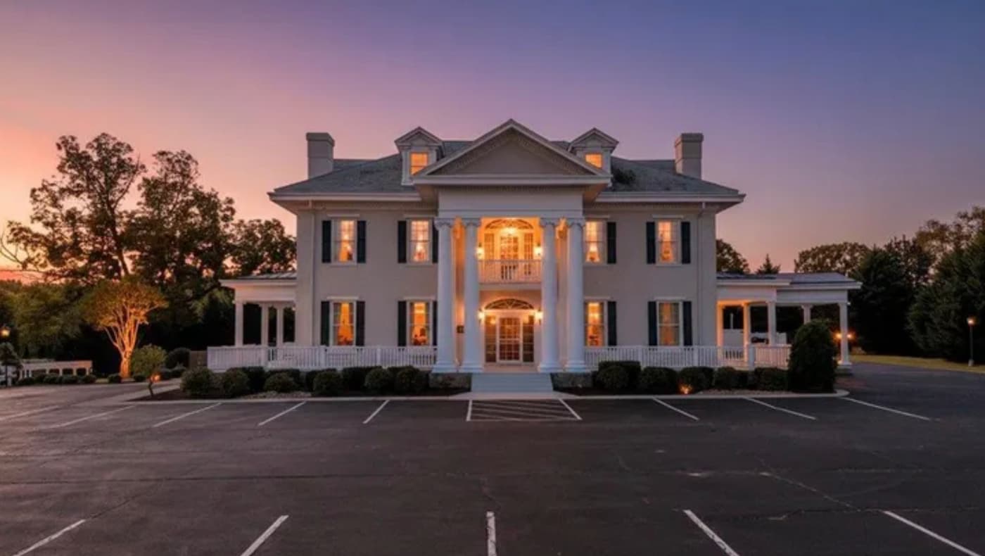 Exterior of "The Bedford Columns," a stately c. 1848 Greek Revival and Colonial Revival estate in Bedford, VA. The three-story historic building features a grand two-story portico with massive white columns, a stucco facade, and a symmetrical design.