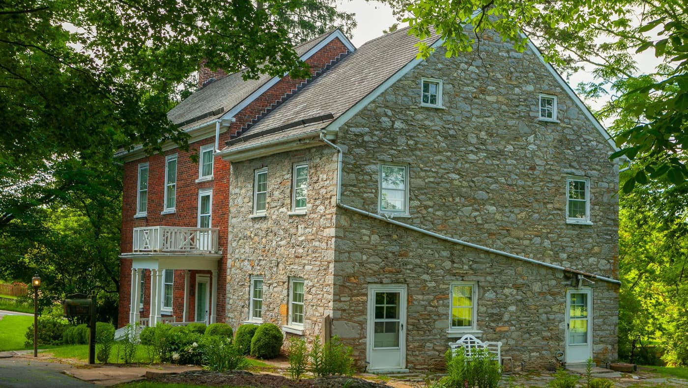 The grand Huxley Hall estate in Martinsburg, WV; a mid-19th-century Greek Revival and Italianate mansion for sale on PreservationDirectory.com, featuring a columned portico, brick facade, and ornate cornices.