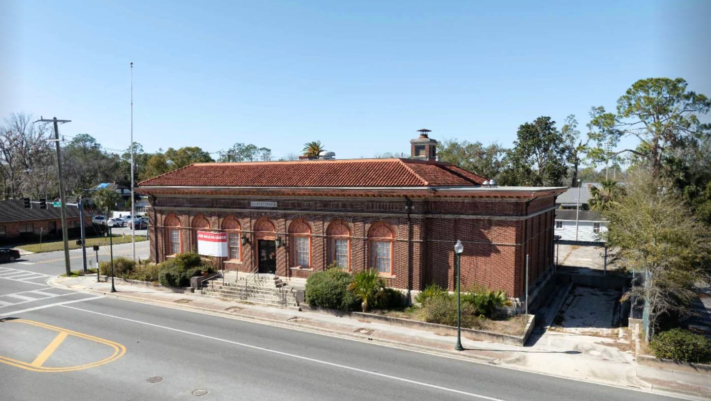 Exterior of the 1915 Historic Post Office in Live Oak, FL, for sale on PreservationDirectory.com. The grand Classical Revival building features a symmetrical red brick facade, a monumental limestone portico with Doric columns, and a terracotta tile roof.