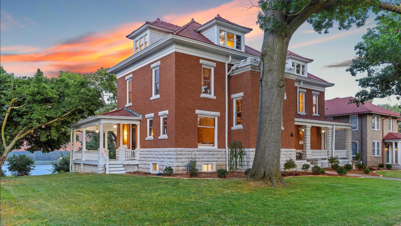 Exterior of the impeccably restored 1902 McFadden House at 729 Grand Avenue, Keokuk, IA. This riverfront estate features a sprawling wraparound porch, a three-story turret, and classic Queen Anne architectural details overlooking the Mississippi River.