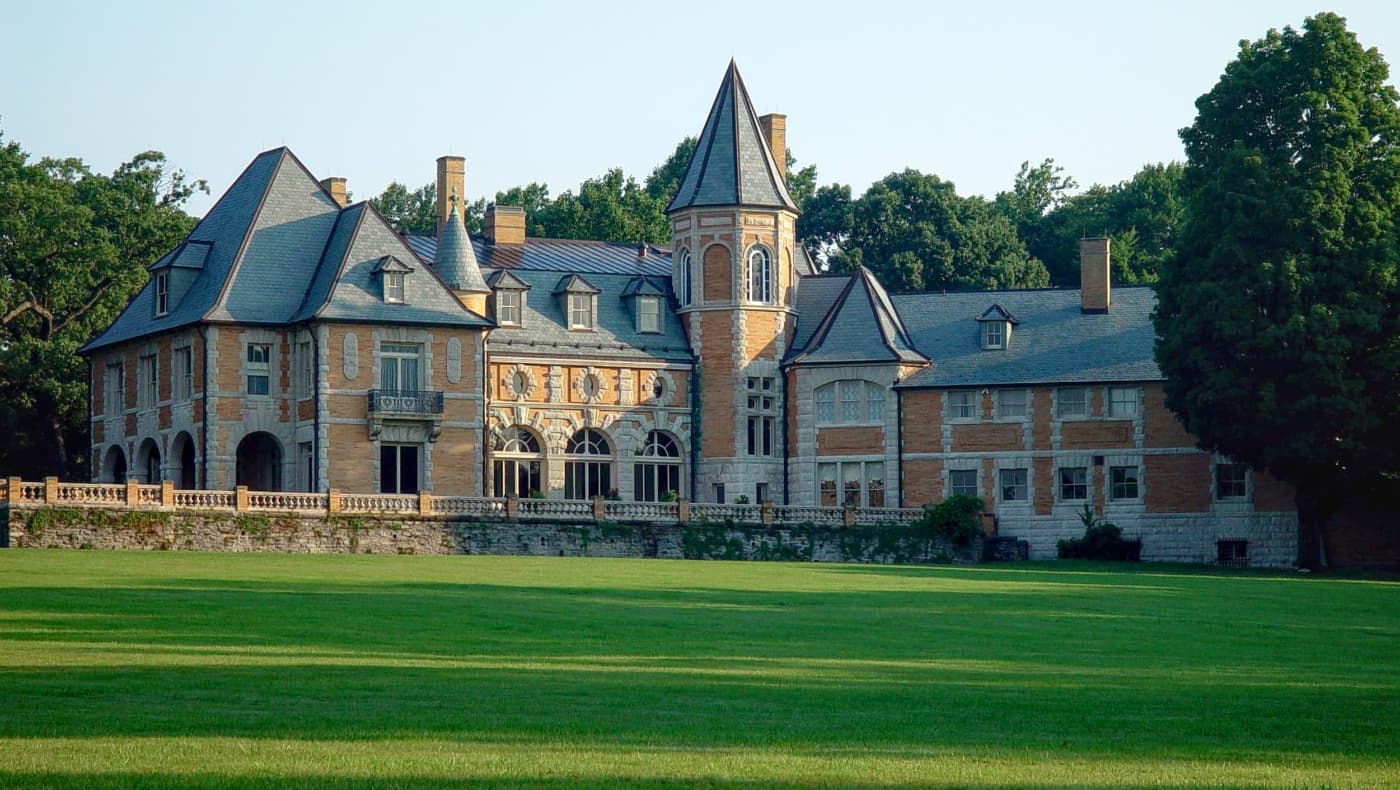 Exterior front facade of Cairnwood Estate in Bryn Athyn, PA. The 1895 Gilded Age mansion, designed by Carrère and Hastings, is a 2½-story Beaux-Arts country house featuring distinct yellow Roman brick, light grey limestone trim, and a symmetrical layout.