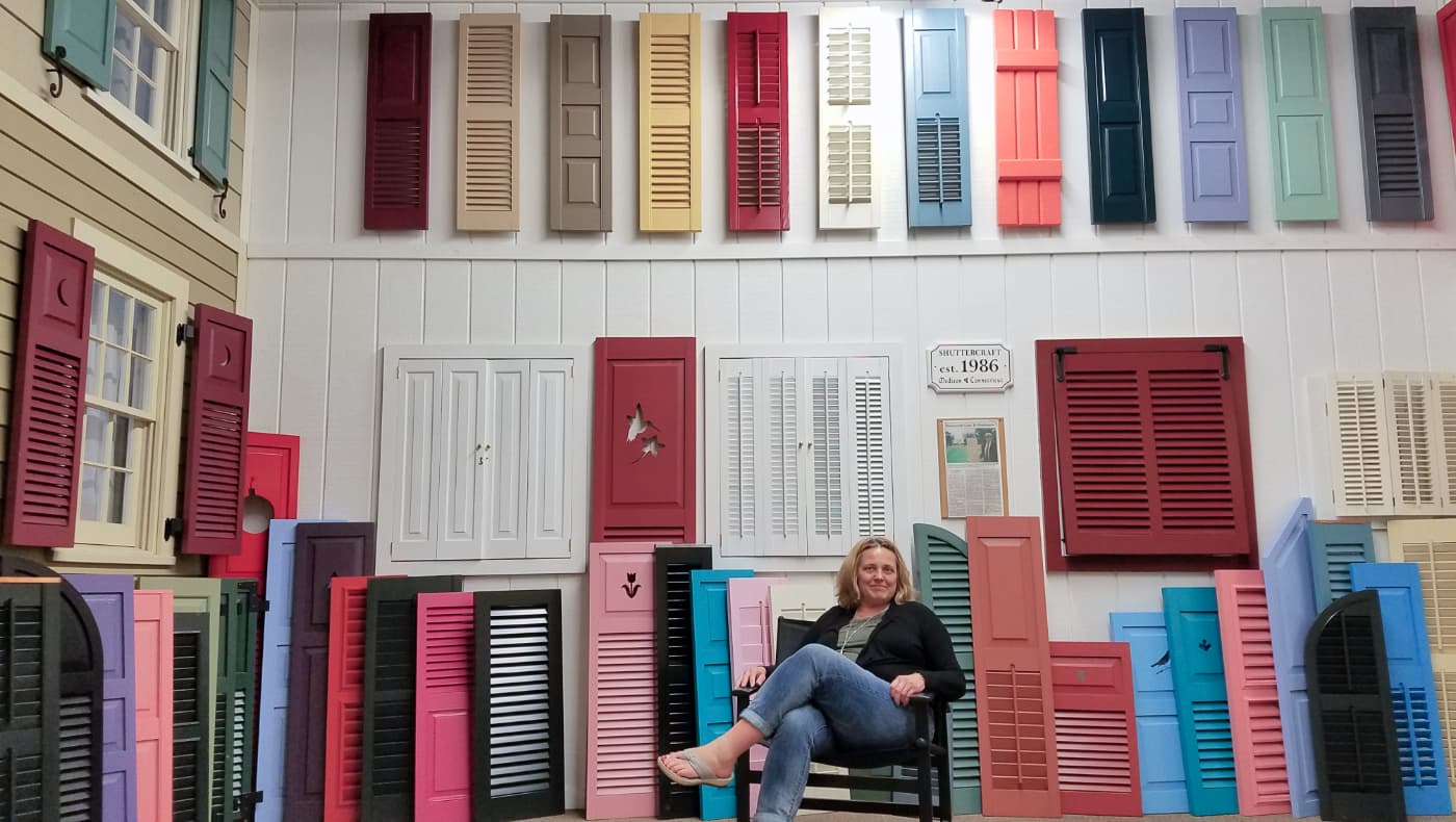 Shuttercraft founder standing in the Madison, CT showroom surrounded by various real wood exterior and interior shutter styles, including Western Red Cedar louvers and raised panels.