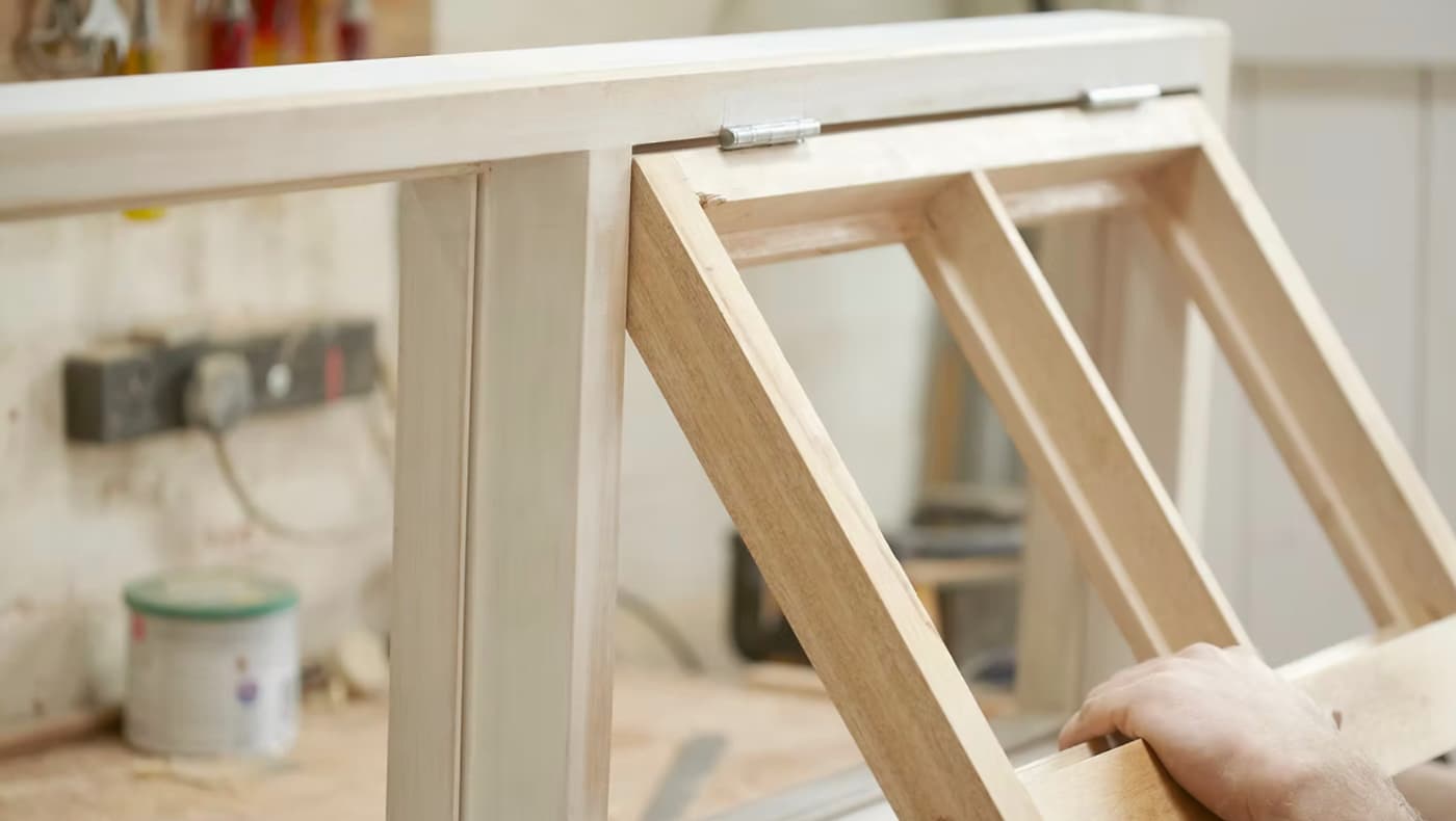 A skilled craftsman at Kinney Woodworks meticulously restores a historic wood awning window. The employee is shown performing precision joinery and frame repair, highlighting the traditional woodworking techniques used to preserve original architectural features.