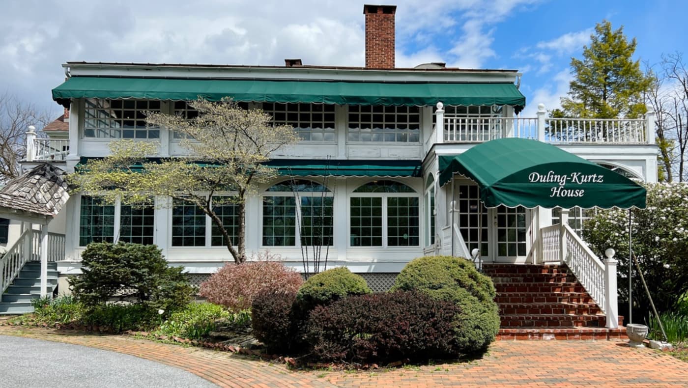 Exterior of the historic Duling-Kurtz House & Country Inn in Exton, PA. The c. 1830 Federal-style fieldstone building features traditional white-trimmed windows, a gabled roof, and a welcoming arched entryway.