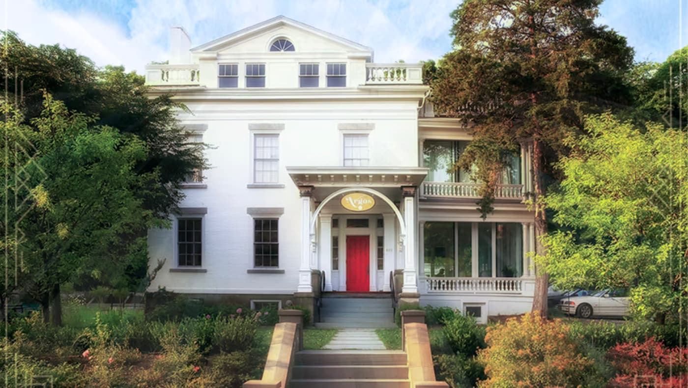 The historic brick facade of Argos Inn in Ithaca, NY, featuring Federal-style architecture, a grand covered porch, and restored masonry.