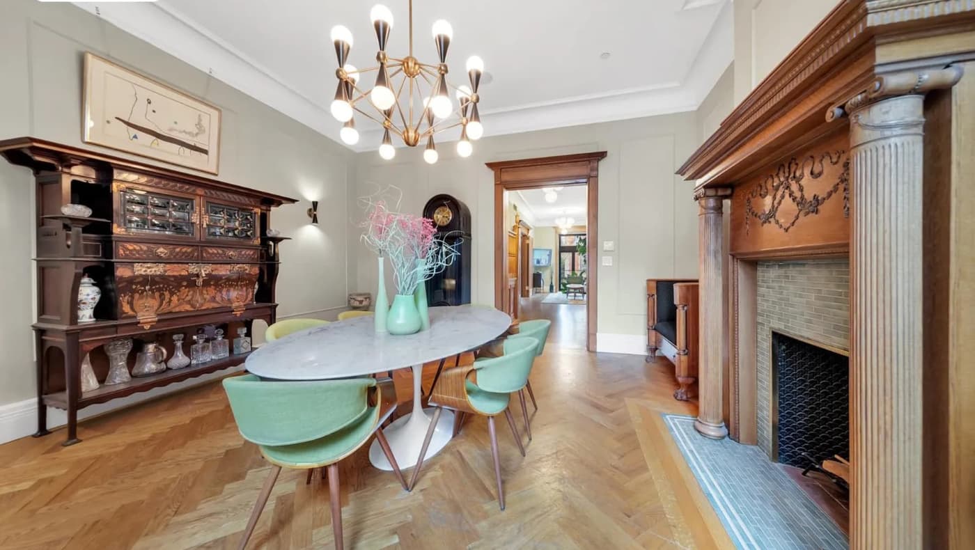 A grand historic dining room in a Striver’s Row townhouse featuring floor-to-ceiling mahogany paneling, an original carved fireplace mantel, and ornate plaster ceiling moldings.