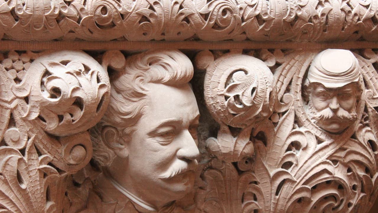 Intricate sandstone carvings of historical faces on the Million Dollar Staircase, New York State Capitol. Detailed 19th-century stonemasonry featuring portraiture and floral scrollwork in Albany, NY.