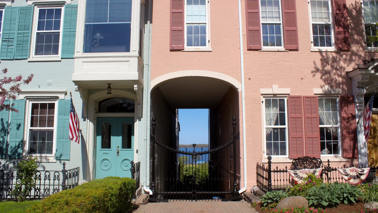 A row of historic Federal-style brick rowhouses in the South Main Street Historic District of Geneva, NY, featuring a unique pedestrian alleyway providing a direct view through the structures to Seneca Lake.