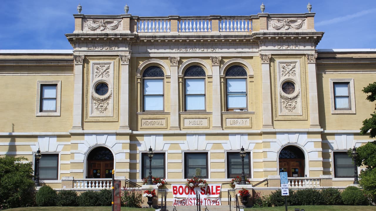 The Adams Free Library in Adams, MA; a grand Beaux-Arts style building featuring a rusticated limestone exterior, a majestic arched entrance, and a prominent copper-domed cupola.