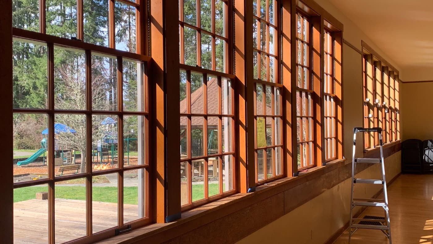 Alt Text: An interior view of a long hallway featuring a series of large, multi-lite wood windows restored by Chosen Wood Window Maintenance.
