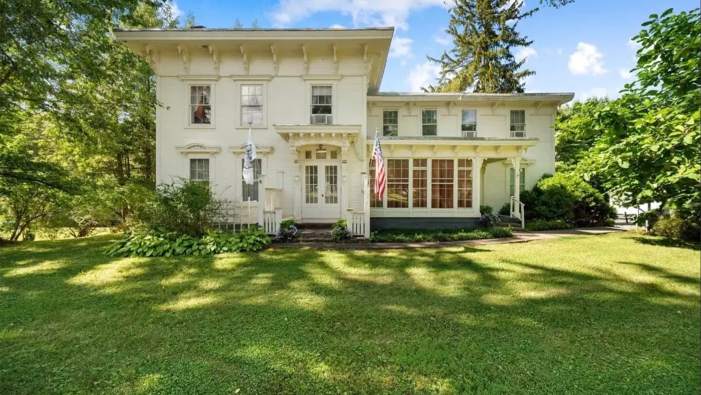 Front exterior of a grand, two-story historic Italianate-style home in Clinton. The residence features a symmetrical facade with tall, narrow windows topped by decorative hoods, a shallow-pitched roof with deep overhanging eaves, and ornate wooden brackets.