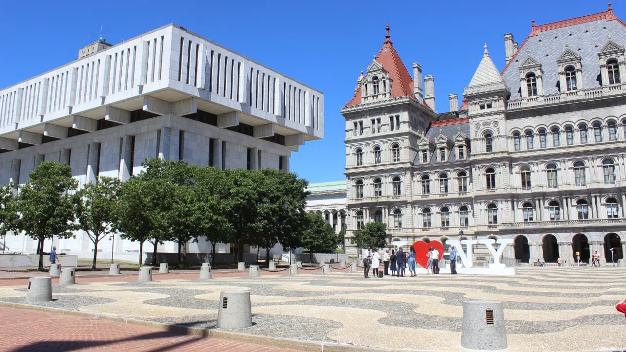 Alt Text: A wide view of the Empire State Plaza in Albany, NY, showcasing the striking architectural contrast between the historic New York State Capitol and the Brutalist Justice Building.
