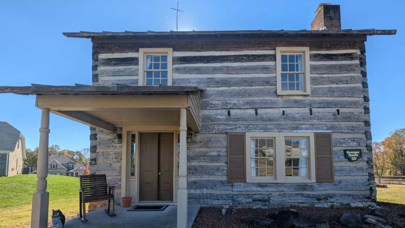 The historic c. 1830 Kreeger Cabin for sale by Preservation North Carolina, showing its two-story hewn-log exterior, front porch, and historic multi-pane windows.