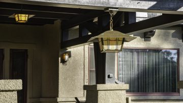 A medium shot of a chain mounted exterior pendant designed after the Gamble House with an aged patina finish and golden glass. It's installed in the porte-cochere of a historic home for one of Brett Waterman's restorations.