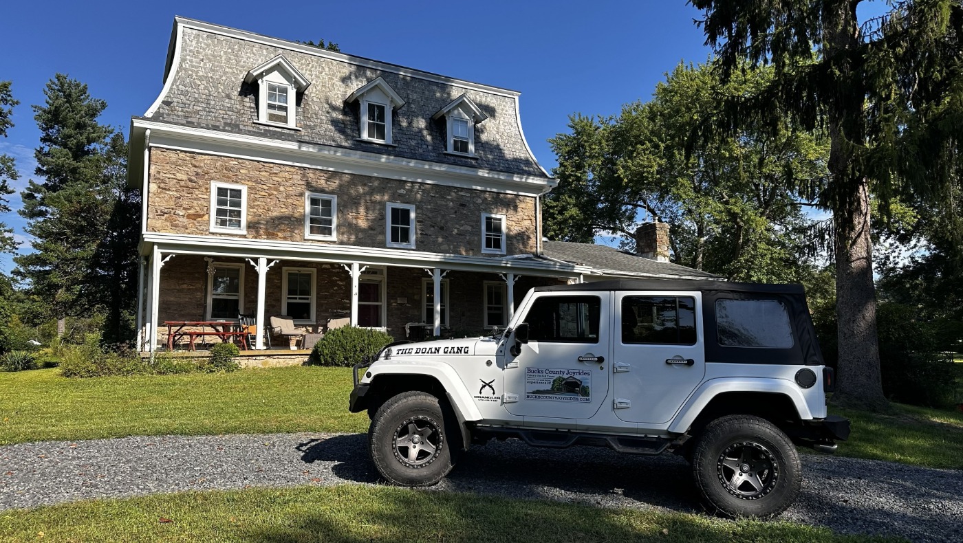 Bucks County Joyrides white Jeep parked in front of a stone house with a mansard roof and front porch in Bucks County, Pennsylvania.