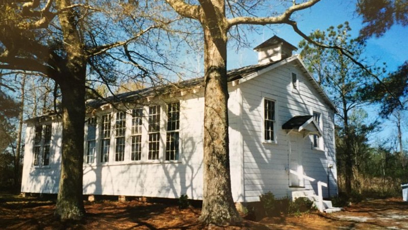 Stanford Community Center in Magnolia, North Carolina: white frame 1942 schoolhouse with a bank of nine-over-nine windows and a louvered bell tower, shaded by oak trees